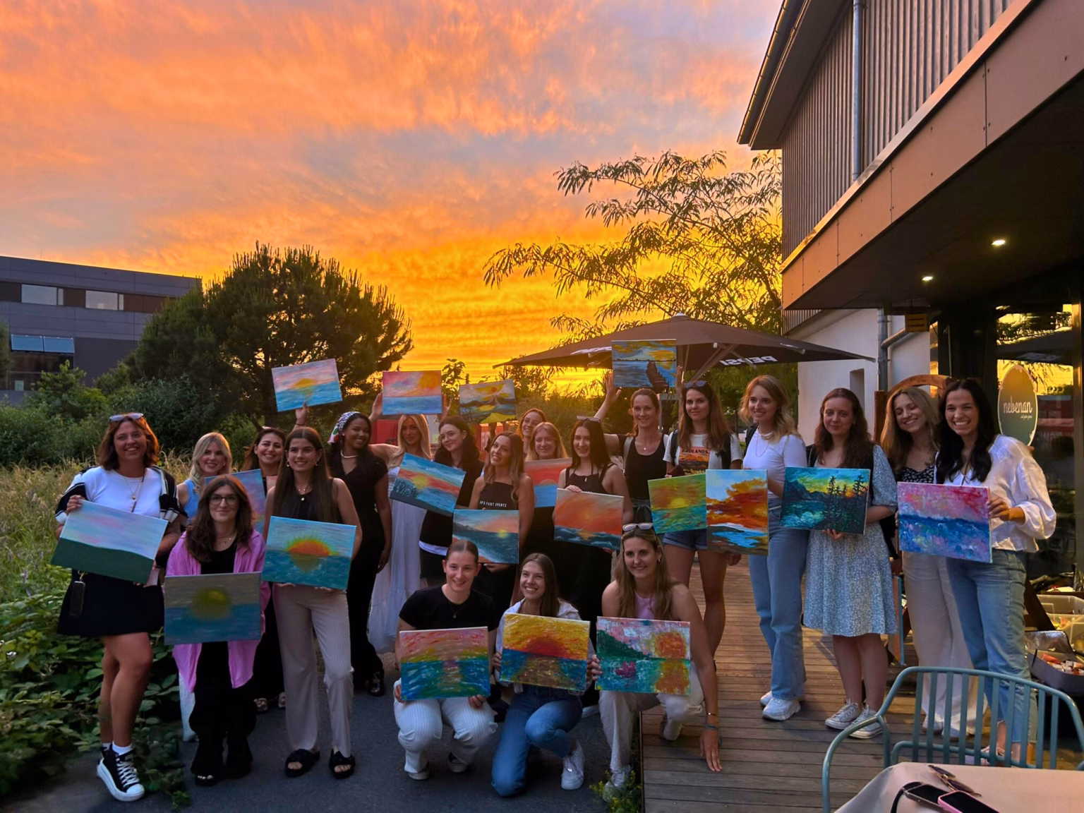 Exklusive Events für Gruppen - hier ist eine Gruppe bei einem Sip & Paint Event - sie zeigen ihre fertigen Bilder vor einem schönen Sonnenuntergang